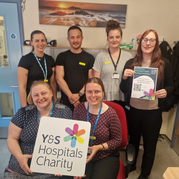 Research and Innovation team smiling, holding our charity logo board