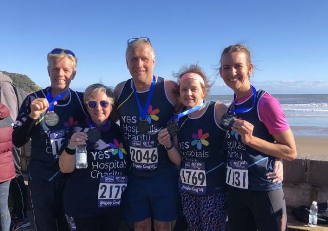 Five runners posing with their medals after completing a run. They are smiling 